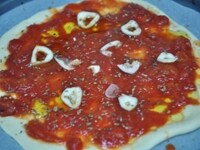 1のピザ生地に2のトマトソースをしき、スライスしたニンニク、乾燥オレガノをまわしかけ、オリーブオイルを軽く回しかけて、200-250℃のオーブンで10～15分焼く。