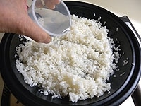 同じくタジン鍋を中火にかけます。サラダ油（残りの分）を加え温まったら米を加え、焦げ付かないように炒めます。水と酒を加え、米が底に付かないように全体をかき混ぜます。<br />
<br />