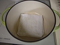 鍋の底に、ゆるく絞った濡れ布巾を敷きます。<br />