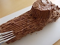 1/6くらいの長さの部分を切り取り、切り株部分にします。切り株部分のケーキの下にチョコレートクリームを塗り、接着します。<br />
<br />
全体にチョコレートクリームをパレットナイフで塗ります。フォークで切り株模様に筋をつけ、お好みでカカオパウダーと粉糖をふります。チョコレートやいちごなどを飾り、出来上がりです。<br />