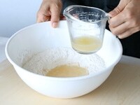 ボウルに米粉、強力粉、塩、砂糖、スキムミルクを入れて、スプーンやゴムベラでよく混ぜる。分量の水から大さじ2をとり分け、残りの水にインスタントドライイーストを混ぜ溶かし、粉のボウルに加える。<br />