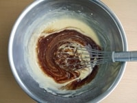 1で溶かしておいたチョコレートとバターを加え、泡立て器で全体が完全に混ざるまでよく混ぜます。<br />