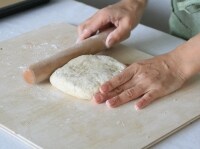 打ち粉をした台に取り出し、粉をまぶした麺棒を生地にあてて四角く形を整える。<br />