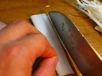 ねぎの白い皮の部分をまな板に押し付けるようにして広げ、包丁で細切りにします。