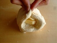 生地を少し広げ、そこにバターを置き、包み込むように練りこんでいきます。バターがなじむまで引き続き5分程度こねます。<br />