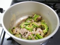 鍋にごま油を熱し、豚肉を加えて炒め、色が変わったら、ゴーヤ、白ゴマを加えます。<br />