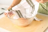 水にぬらして固く絞った布巾をかぶせ、28℃くらいの室温で50分、オーブンの発酵機能を利用するなら、30℃に設定して40分ほど一次発酵させる。<br />