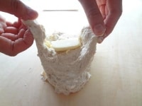生地を少し広げ、そこに無塩バターを置き、包み込むように練りこんでいきます。無塩バターがなじむまで引き続き5分程度こねます。<br />