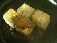 豆腐の上から酒をふりかけ、醤油を回しかけ、箸で転がしながら香ばしく焼きつけて火を止める。<br />
<br />