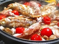 そこにパプリカ以外の具、つまり鶏肉、魚、ヤリイカ、よく洗ったアサリ（砂抜きしていないものはあらかじめ砂を抜いておく）、トマトを並べます。 このときトマトとアサリ、鶏肉は米の中に押し込むようにし（トマトはつぶれても一向にかまいません）、魚とヤリイカは米の上に置くようにします。 ときどき鍋を回し、全体に満遍なく火が当たるようにします。 火加減はガスコンロの弱火程度になるよう調整します。