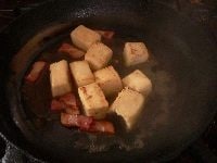 高野豆腐の表面を焼いたら、調味料（おおよその分量：水 大さじ3、酒 小さじ1、みりん 小さじ1、砂糖 小さじ1、醤油 小さじ2）を加え、転がしながら煮る。 <br />