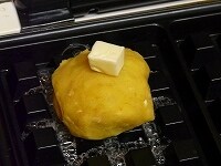 ワッフルメーカーにバター（分量外）をのせて丸めた生地を載せる。そのうえにさらにバターを載せてふたを閉じ、軽く焦げ目がつくまで焼く。