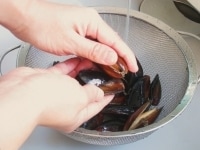冷凍のムール貝をボウルにあけ水に1分ほど漬けます。流水の中で殻と殻をこすり合わせ汚れをとります。<br />