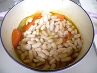 8等分に切ったトマトも加え炒め、白花豆の水煮缶を煮汁ごと加えます。<br />