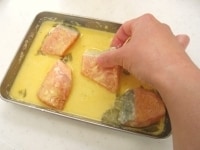 バットに卵と牛乳、粉チーズを入れ、フォークを使って卵の白身をくずすようにして全体を混ぜ合わせます。そこに鮭を入れて卵液をからめていきます。