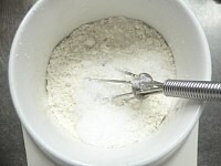 マグカップに薄力粉とベーキングパウダーを入れ、泡だて器でグルグル混ぜ、砂糖と塩を入れてグルグル混ぜる。<br />