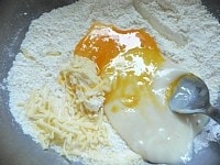 ボウルに薄力粉、ベーキングパウダーを入れ、泡だて器でグルグル混ぜ、砂糖と粉チーズを加えて混ぜる。次に餅、卵、ピザ用チーズを加える。<br />