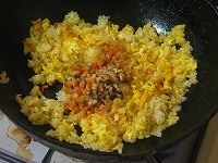 割りほぐした卵を鍋に注ぎ入れ、すぐにご飯を入れて中華ヘラなどで手早くかき混ぜる。卵とご飯がだいたい均等に混ざったら、干しエビ、干しシイタケ、ザーサイを加え、さらによくかき混ぜる。