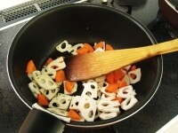 鍋にごま油とおろしたニンニクを入れ加熱し、れんこんとにんじんを入れて1分程炒めます。<br />