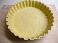 型にバター（分量外）を塗り、パイ生地を型に押しつけ形を整え、端を落とします。底面全体にフォークの先で穴を開けます。