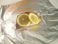 アルミホイルの中央に、表面の水気を拭き取った鯛1切をおき、スライスしたレモンを2枚のせます。酒、醤油を加え、タイムをふって四方を包みます。<br />