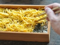 寿司飯を器に盛り付けたら、その上にきざみ海苔といりごまを振りかけ、錦糸卵をふんわりと盛り付けます。<br />
