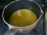 手鍋にグラニュー糖とオレンジジュースを入れ、火にかける。グラニュー糖が溶けたら、火からおろしボウルに移す。<br />
