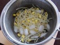 大豆もやしをボウルに張った氷水で一気に冷やして熱を取ります。熱が取れたら、水を2-3度替えて洗います。こうすることで、もやしの独特の苦味が抜けます。<br />
<br />
洗ったもやしは水気を切って、かたく絞ります。<br />