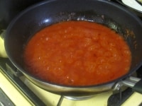 水煮トマトはボールに入れて手で潰しておく。ニンニクとオリーブオイルを入れたフライパンを火にかけ、香りが出たら水煮トマトを加えて煮詰め、塩で調味する。