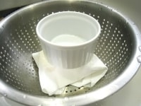 木綿豆腐をペーパータオルなどにくるみ、ザルの中に入れて上から重しをのせます。5分ほど置き、豆腐から余分な水を出します。<br />