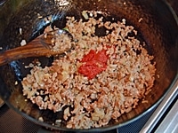フライパンにオリーブオイル、ニンニクを入れて火にかけ、香りがでたら玉ねぎを炒め、しんなりしたらひき肉を加える。<br />
肉の色が変わり、水分がなくなったらトマトペーストを加えて炒め、パプリカ、トマト、ピーマン、水の順に加える。