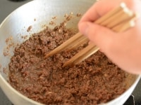 箸で混ぜ続けると、肉がだまにならずに火が通ります。調味料や肉の水分が出てくるため、混ぜる手を少しゆるめ、出てきた汁気を飛ばします。