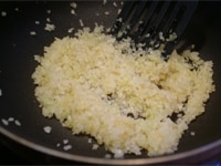 フライパンにオリーブオイルを入れ、ニンニクを炒め、香りが立ったら玉ねぎを加え、透明になるまで炒めます。さらに米を入れて、表面が透き通るようになるまで炒めます。