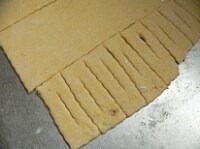 打ち粉をふった台の上に置き、麺棒で2～3ミリ厚に伸ばす。パイカッターで長方形に切り、真ん中に切り込みを入れる。<br />