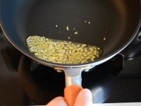 フライパンに大さじ2のオリーブオイルを入れて弱火にかけ、みじん切りにしたにんにくを入れて、香りが出るまでじっくり炒めます。