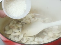 マッシュルームに油が回ったら洗っていない米を加えて炒める。水にスープの素を加えて温めて溶かし、スープを作っておく。