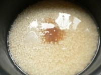 おこわ用の目盛りの3の線まで水を足し、塩と砂糖（きび砂糖使用）を入れて軽く混ぜる。<br />