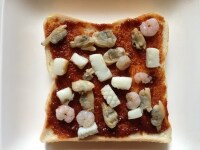 パンにソースを塗り、シーフードミックを並べ、ピザ用チーズをのせて、トースターでチーズが溶けるまで焼く。<br />