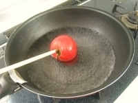 鍋に水を入れて沸騰させます。菜箸にトマトを刺し、湯の中で転がします。冷水にとって皮をツルツルとむいていきます。<br />