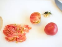 トマトは半分に切って、ヘタの部分を三角に切り落とし、角切りにします。<br />
