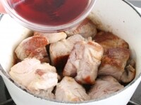 鍋にオリーブ油を熱し、豚肉を炒める。肉にこんがりと焼き色がついてきたら赤ワインを加える。