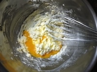室温に戻しておいた卵をときほぐし、2～3回に分けて加え、そのつど、泡立て器でよく混ぜます。