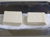 キッチンペーパーで豆腐を包み、お皿などを使って重石（500g）を30分ほどかけて水気を切ります。<br />