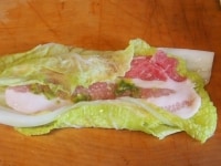 白菜の葉を２枚重ね、そのうえに豚バラ肉を置き、柚子胡椒を塗る。縁を折りたたんでから、巻く。