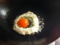 お好みでガパオ炒めの付け合わせの目玉焼きを作る。たっぷりの油を熱し、卵を割り入れ、卵の上から熱々の油をかけながら焼く。<br />