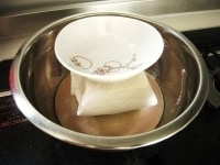 ボウルの中に平皿を逆さにして入れます。この上に、ペーパータオルなどで包んだ木綿豆腐をおき、上に重し(小皿など）をのせます。7～8分ほどおいて水切りします。