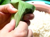 手前に折った笹の葉で米を覆ってかぶせ、葉の真ん中を山折りにする。<br />