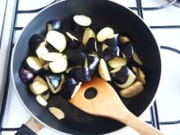 フライパンにオリーブオイル（大さじ２）、ニンニクを加えて弱火にかけます。香りが出たら、なすを加えて中火でよく炒めます。