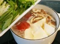 トマトが柔らかくなったらしいたけ・豆腐を加え、火が通ったら塩を加えて調味し、九条ねぎ・水菜を加える。