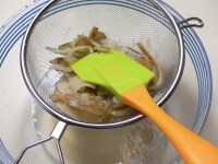 ボウルにザルを重ね、ゴムベラでこして、芋の白い部分を煮汁の中に落とす。<br />